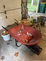 Red plastic wheelbarrow from front left angle showing the basin, frame, and wheel