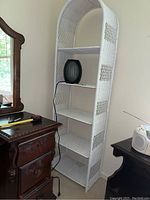 White wicker shelving unit against wall with a small black fan on one shelf, wooden dresser to the left, and stereo unit to the right.