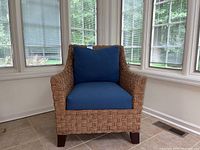 Front view of woven rattan armchair with navy cushions showing entire chair with wooden legs