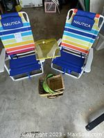 Two Nautica brand beach chairs with striped fabric, yellow mesh food cover on a chair arm, and three wicker baskets on the floor below.
