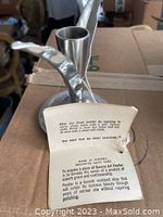 Close-up of one pewter candle holder with attached label detailing care instructions and origin at Brooklyn Navy Yard.