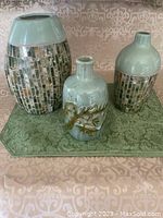 Front view of three decorative vases shown on green patterned mat, two mosaic inlay with green glaze tops, one ceramic with raised leaf design.