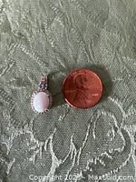 Top view of oval opal pendant next to a penny for scale, showing the front with opal and accent stones on silver setting.