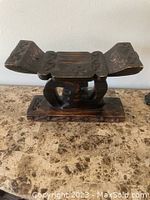 Front view of carved Ashanti wooden headrest showing double-raised design, geometric carvings, and wood grain wear.