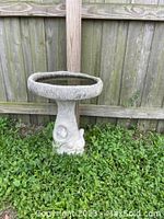 Concrete birdbath placed outdoors on grass, showing the full birdbath structure with round basin and carved pedestal base.