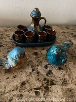 Photo showing the full set of blue ceramic wine decanter with eight small cups on tray and two blue ceramic bird figurines on marble surface.