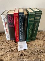 Photo of nine books with varied topics including real estate, literature, and contracts, arranged upright on a wooden surface.