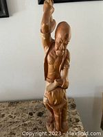 Front and side view of the carved wooden statue showing detailed muscular man holding an object raised above his head.