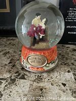 Front view of the globe showing the couple figurine inside and the decorative base with flames and plaque.