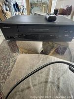 Front view of the black Daewoo DV-T3DN video cassette recorder with remote control on top, showing the tape slot and buttons.