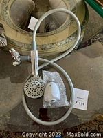 Photo of the Earth shower head connected to a flexible metal hose laid out on a reflective surface.