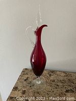 Full view of the tall ruby red crystal decanter with twisted clear handle and clear glass stopper standing on a marble surface.