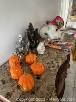 View of carved ceramic pumpkins, haunted house figurine, ghost, and black tree candle holder on marble surface