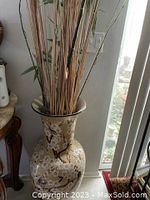 Full view of large Asian ceramic vase with floral and bird design filled with tall bamboo stalks and dried reeds.