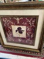 Front view of framed picture showing central iris flower design on burgundy background with decorative scrollwork and ornate carved frame.