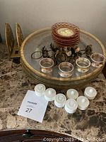 Photo of all items including glass plates stacked in center, metal floral napkin rings, and glass candle holders arranged on a large tray.