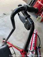 Photo showing the handle of the red rolling walker with brake lever and black handgrip.