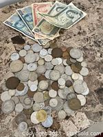 Mixed old coins and paper money laid out on a stone surface, showing a variety of coins and Canadian and Mexican currency.