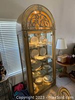 Full view of the tall lighted wood and glass display cabinet with ornate metal decorations and interior lighting showing dishes.