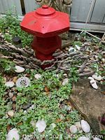 Red painted pagoda structure situated outdoors on gravel and plants
