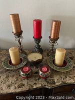 Overview of seven assorted candles and candle holders on a marble surface, including three pillar candles and four types of holders made from metal and ceramic.