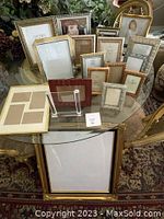 Photo of a collection of assorted picture frames in various sizes and styles arranged on a glass table, showing gold, silver, and wood finish frames.