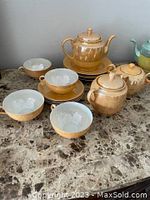 Full set on marble table showing teapot, sugar bowl, creamer, tea cups, saucers, and side plates with peach lusterware finish.