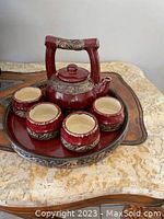 Full view of the tea set on the tray, showing teapot, four cups, and tray with carved decorative patterns in red glaze.