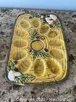 Front view of the vintage mushroom and leaf ceramic egg tray showing the yellow textured base with three clusters of raised mushrooms, leaves, and acorns arranged around the tray.