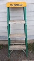 Full frontal photo of the Green Featherlite 4-foot step ladder showing three aluminum steps and yellow top cap with brand name.