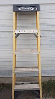 Full view of the Werner 5-foot fiberglass step ladder showing its yellow fiberglass rails and aluminum steps against a garage door.