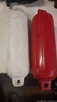 Photo of two approximately 16 inch boat bumpers, one white and one red, showing their tubular shape and rope eyelets at both ends.