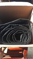 Tightly folded black mesh tarp inside an open cardboard box showing the coiled tarp material.