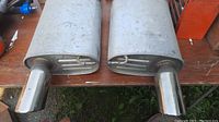 Pair of factory mufflers placed side by side showing rectangular shapes and polished exhaust tips.