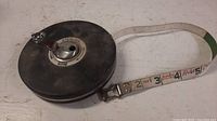 Photo showing the black metal reel casing of Lufkin tape measure, with white fibre tape extended showing red and black numbers.