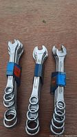 Photo of three bundles of combination wrenches. The wrenches are chrome finished and held with blue or red straps. The sets are arranged upright, showing different sizes in each set.