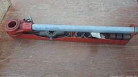 Full view of manual pipe threader with attached metal handle and red metal tray containing threading dies underneath.