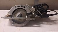 Side profile of Skilsaw Wormdrive 7 1/4 inch circular saw showing blade guard with 'SKILSAW' branding and power cord.