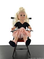 Front view of the 18 inch doll seated on a wooden chair, showing full body and outfit