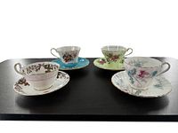 Angle view showing all four different floral bone china cup and saucer sets arranged on black surface