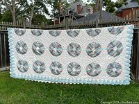 Full view of quilt hung on clothesline showing multiple rows of Dresden Plate circular patchwork patterns on a white quilted background with blue scalloped edges.