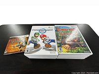Photo showing stacks of Nintendo Wii game cases on a table including Mario Kart Wii, Donkey Kong Country Returns, and others, with game manual for Link's Crossbow Training visible.