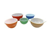 Front view of all five mixing bowls arranged from left to right: orange Pyrex Autumn Harvest Wheat bowl, bright red vintage Pyrex bowl, small green Fire King bowl, blue Pyrex Cinderella bowl, beige Pyrex mixing bowl with lift handles.