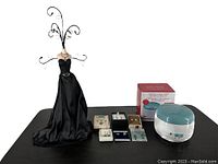 Black satin mannequin jewelry holder with multiple curved wire branches for hanging earrings and necklace, shown with all earring sets and jewelry cleaner arranged on table