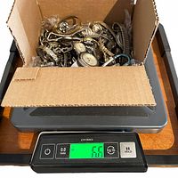 Box filled with assorted vintage wristwatches on digital scale showing weight 6.6 pounds.