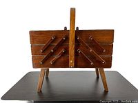 Front view of vintage wooden 3-tier expandable accordion sewing box closed with handle and legs extended.