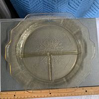 Top view of one amber-colored divided glass plate showing the scalloped edges, three compartment dividers, and the detailed filigree etched pattern.