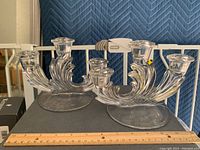 Pair of clear pressed glass tri-candelabra, viewed from the side showing the swirl design and round bases with a ruler for scale.