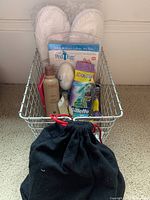 Photo of metal basket containing foot care items including slippers, Ped Egg, shampoo, razors, curlers, and grooming scissors with black pouch in front.