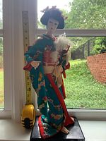 Front full-body view of the doll near a window with measuring tape showing height approx 17.5 inches